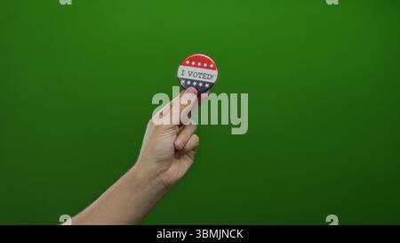 Man holding voting badge against green background symbolizes civic engagement in elections showing hand and pin. Stock Photo