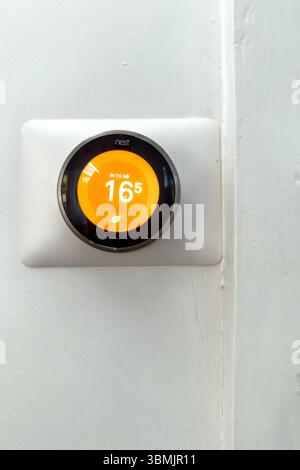 A Nest smart home thermostat mounted on a white wall displaying the temperature set to 16.5 degrees Celsius - heating energy bills home technology Stock Photo