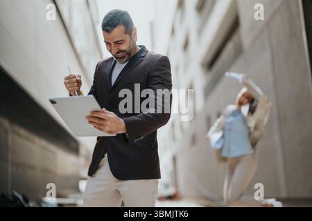 Man celebrating success with a tablet outdoor while a woman joyfully reacts in the background Stock Photo