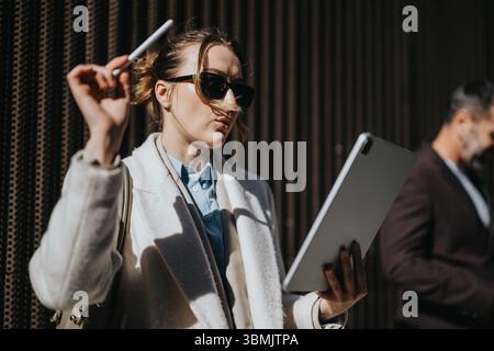Confident businesswoman analyzing tablet data outdoors while holding a pen Stock Photo