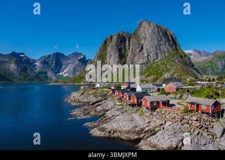 Nestled between steep mountains and crystal-clear waters, a charming fishing village in Lofoten showcases traditional red cabins reflecting vibrant Norwegian culture. Stock Photo