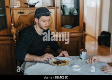 Man preparing a chocolate spread on a pancake in a cozy home environment Stock Photo