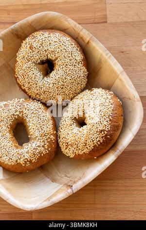 3 hand-made sesame seeded bagels, traditional Jewish bread rolls in a wooden bowl on a wooden chopping board Stock Photo