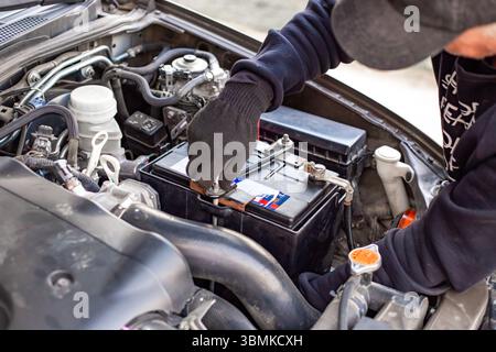 A man wearing gloves disconnects a battery terminal by loosening the clamp. Replacing a battery on a car. Stock Photo