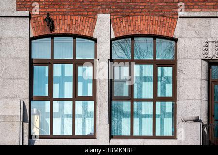Two rectangular windows with a red brick arch against a grey block wall. From the Windows of the World series. Stock Photo
