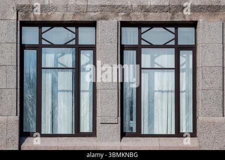 Two rectangular windows with brown frames against a wall of grey blocks. From the Windows of the World series. Stock Photo