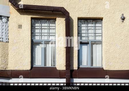 Two rectangular windows on a beige wall with a brown rectangular drainpipe. From the Windows of the World series. Stock Photo
