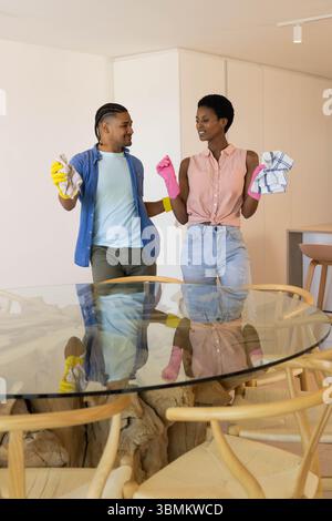 Cleaning diverse couple wiping round glass table in modern kitchen, with yellow and pink gloves Stock Photo