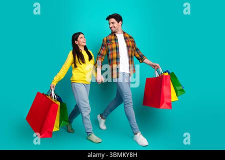 Young couple holding colorful shopping bags and walking on a bright turquoise background showing happiness and joy Stock Photo