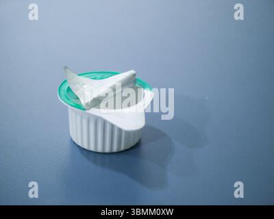 Coffee whitener opened and made of plastic. The container is sitting on a blue surface Stock Photo