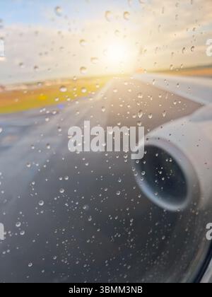 A plane's wing is seen through a window with raindrops on it. The wing is on the right side of the plane Stock Photo