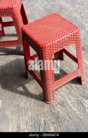 Two red plastic stools are sitting on a wooden floor. The stools are identical in size and shape Stock Photo