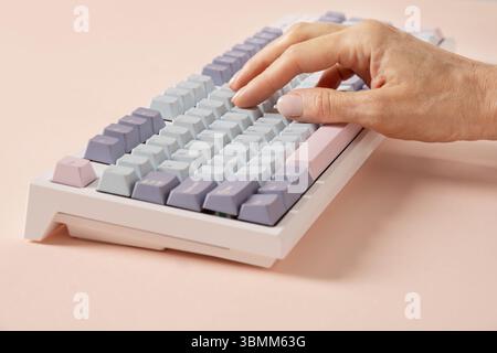 Womans hand typing on mechanical keyboard on pink background. Close up. Stock Photo