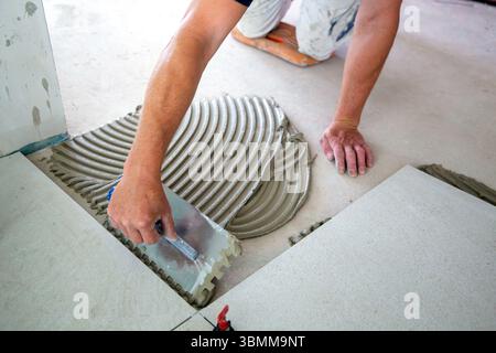 Tile laying: Tiler lays large light-coloured floor tiles Stock Photo