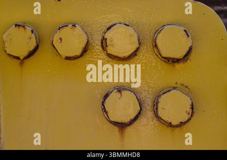 Close-up of six large rusty bolts on a yellow flange showing the old paint and dust bleeding. Stock Photo