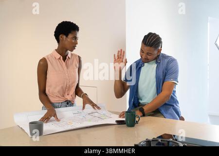 Diverse coworkers examining large blueprint in design studio, with mugs and smartphone Stock Photo