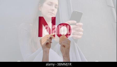 Sitting adult woman holding smartphone at chest level against grey wall, with red no text overlay Stock Photo