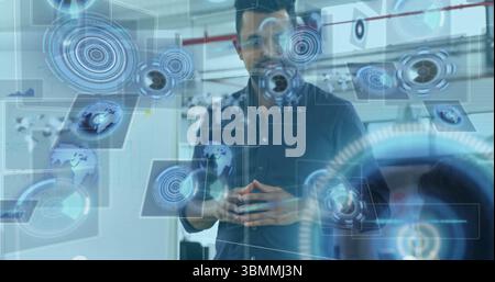 Standing South Asian man interacting with holographic UI in tech lab, with data overlay Stock Photo