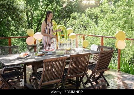 Asian woman decorating wooden dining table on deck for birthday party with balloons and cupcakes Stock Photo