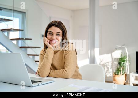 Happy older woman with laptop sitting at home table looking at camera, portrait. Stock Photo