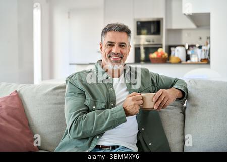 Happy middle aged man holding coffee cup relaxing on couch at home. Portrait. Stock Photo