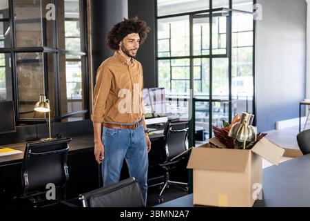 Man standing at workstation in open-plan office unpacking box with lamp and plant, copy space Stock Photo