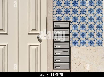 A close-up of a modern apartment entrance with multiple silver mailboxes and traditional blue and white Portuguese azulejo tiles on the facade. Stock Photo