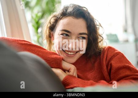 Young happy dreamy woman relaxing sitting on couch at home, dreaming. Stock Photo