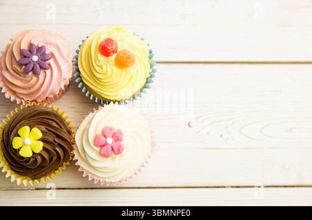 Showing four cupcakes on tabletop, showcasing pastel frosting, fondant flowers, gummies Stock Photo