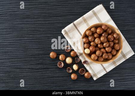 Wooden plate with macadamia nuts on black table. Space for text Stock Photo