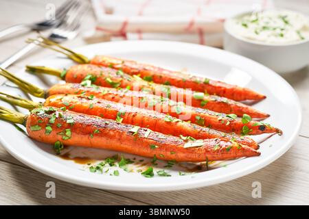 Fried carrot with sauce in a plate on a white wooden table,selective focus. Healthy root vegetables concept. Stock Photo