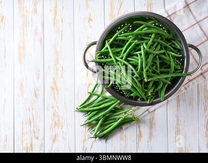fresh green beans in a stainless steel colander on a white wooden table, top view. Stock Photo