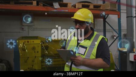 Industrial technician wearing hard hat and vest holding tablet inside warehouse with digital icons Stock Photo