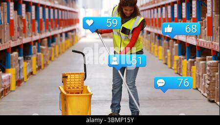 Mopping floor, woman wearing safety vest in warehouse aisle with mop bucket, floating social icons Stock Photo