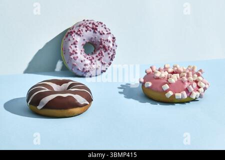 Close up photo of three sweet tasty donuts in caramel and chocolate icing, on a blue background. Mock up, two-colored pastel Stock Photo