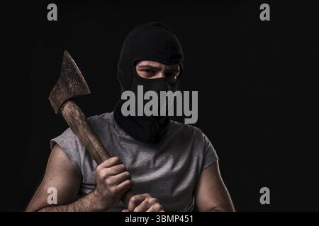 Bandit in black mask with hatchet on black background. Masked man with an ax Stock Photo