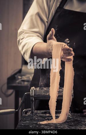 The chef makes fresh spaghetti from scratch. Wooden table. Photo in brown tones. Kitchen Stock Photo