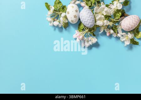 Easter composition with colorful eggs and flowers of apple tree on a blue background. Spring concept, flowers composition. Greeting card. View from ab Stock Photo