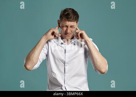 Studio portrait of a smartly dressed young businessman in a classic white shirt acting like he does not want to hear something while posing over a blu Stock Photo