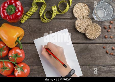 Concept diet, slimming plan with vegetables top view mock up. A female hand in a sports bracelet writes an article about proper nutrition Stock Photo