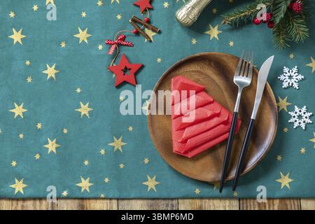 Table setting for Christmas dinner, holiday composition. Table fork and knife set with red paper napkin and fir branch on a rustic celebrate table. To Stock Photo