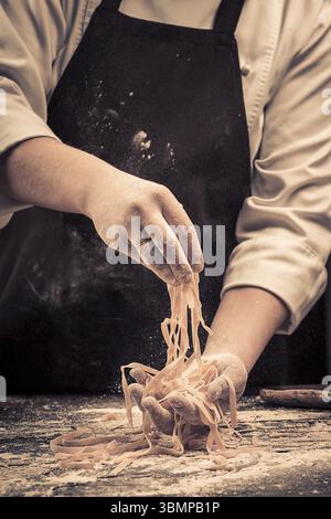 The chef makes fresh spaghetti from scratch. Wooden table. Photo in brown tones. Kitchen Stock Photo