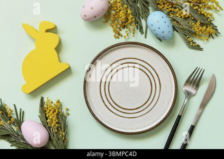 Easter table setting. Plate with easter eggs and mimosa on a pastel green background. Happy Easter holiday concept for restaurants. View from above Stock Photo