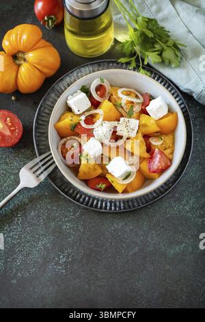 The concept of vegan or diet food. Tomato salad made from a mix of red and yellow tomatoes and feta cheese on a stone tabletop. Copy space Stock Photo