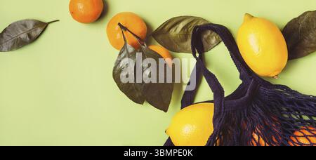 Set of citrus in mesh textile bag on green background Stock Photo