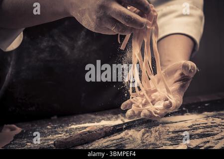 The chef makes fresh spaghetti from scratch. Wooden table. Photo in brown tones. Kitchen Stock Photo
