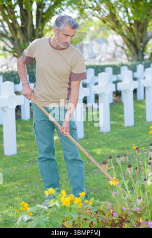 Man hoeing flower beds next to graves Stock Photo