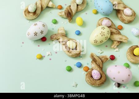 Colors Easter eggs with Easter rabbit-shaped buns puff pastry with cinnamon on pastel green background. Happy Easter Holidays Stock Photo