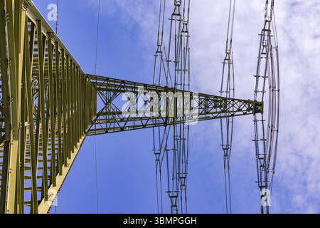 Massive and large high voltage pylon for electricity as power line for many overhead lines against blue sky with view upwards Stock Photo