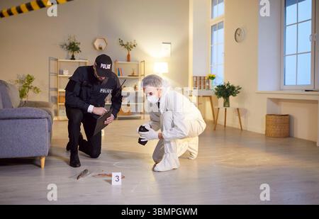 Police detective and forensic scientist looking for evidence at indoor crime scene Stock Photo